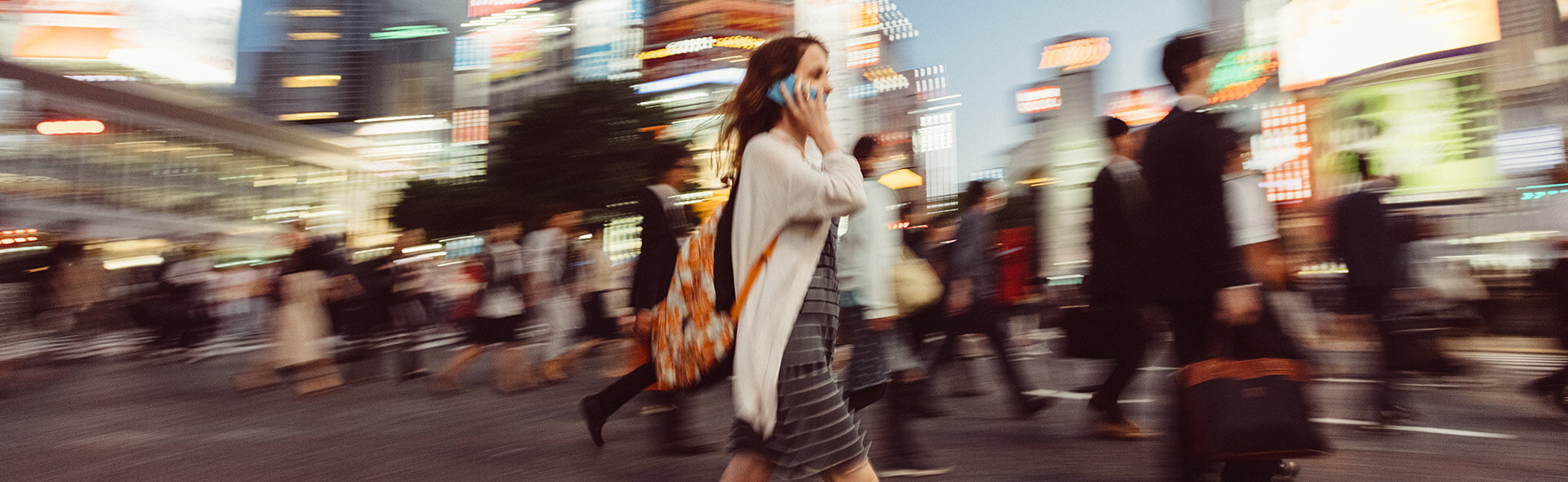 Une femme au téléphone traverse la rue d'une grande ville avec beaucoup d'autres personnes